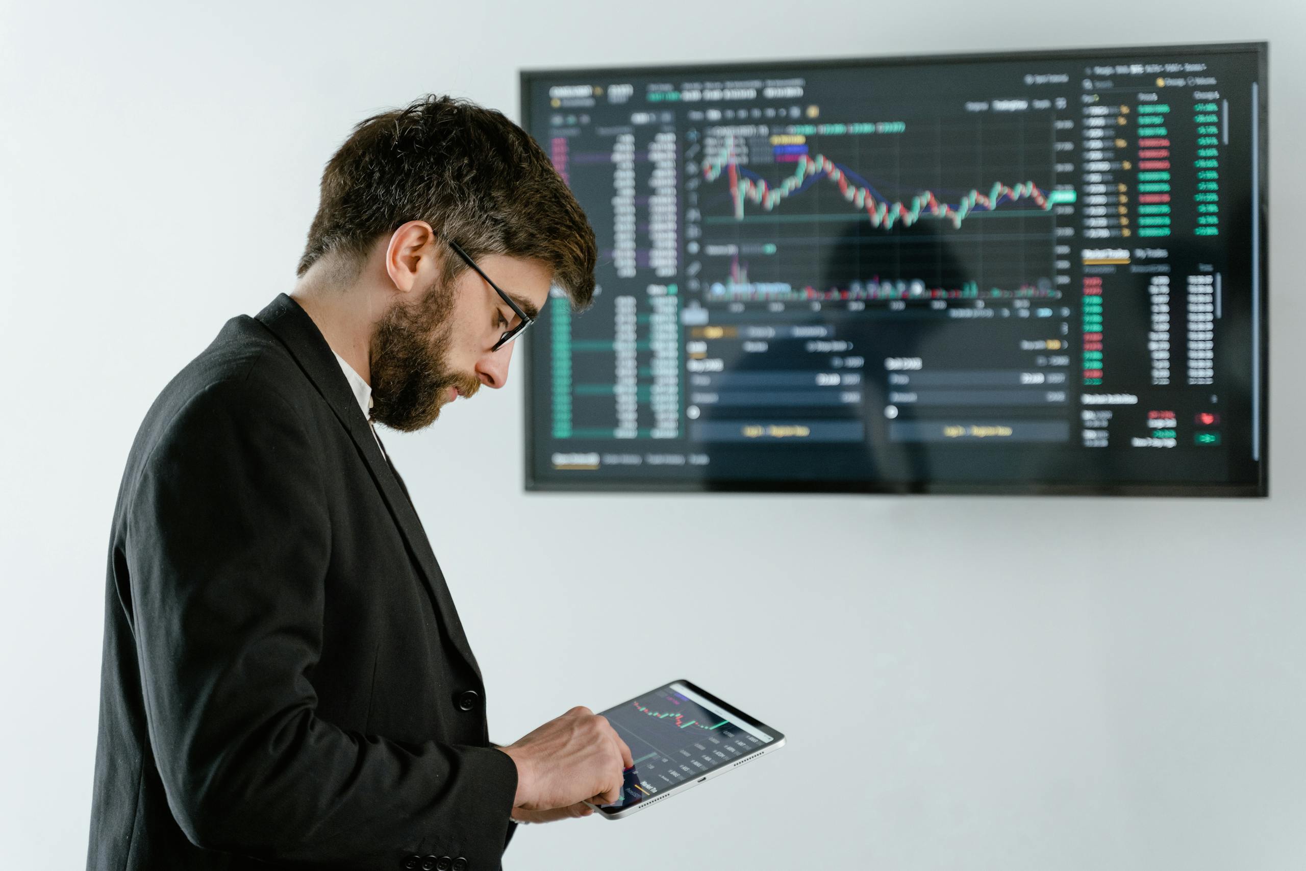 Professional man using tablet in front of cryptocurrency trading screen indoors.